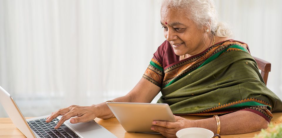 Senior Indian woman learning how to use digital tablet and laptop
